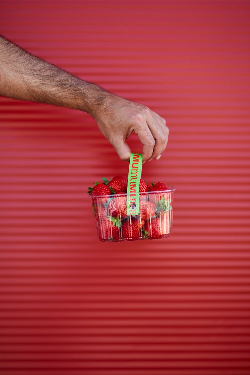 Fotografía en la que se ve una cesta de medio kilo de fresas de mumu en una pared de color corporativo